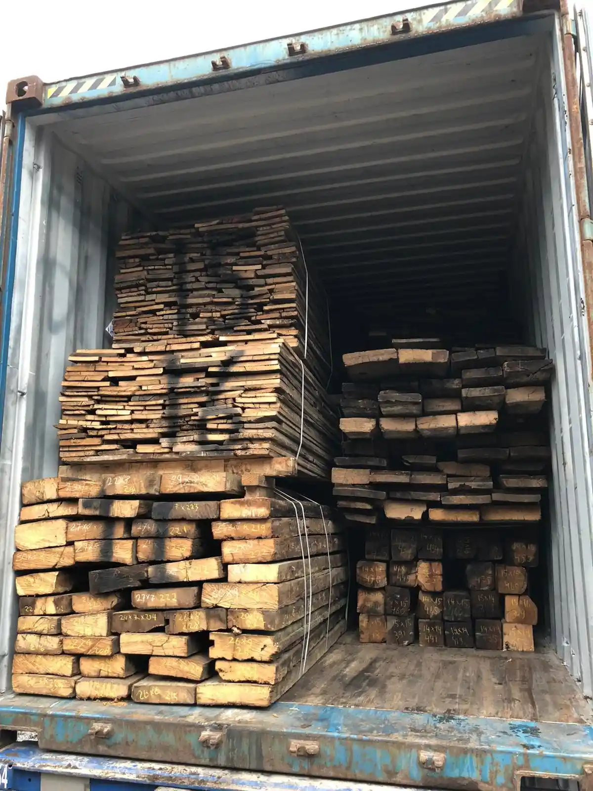 Stacks of reclaimed timber beams with weathered wood textures stored in an outdoor warehouse