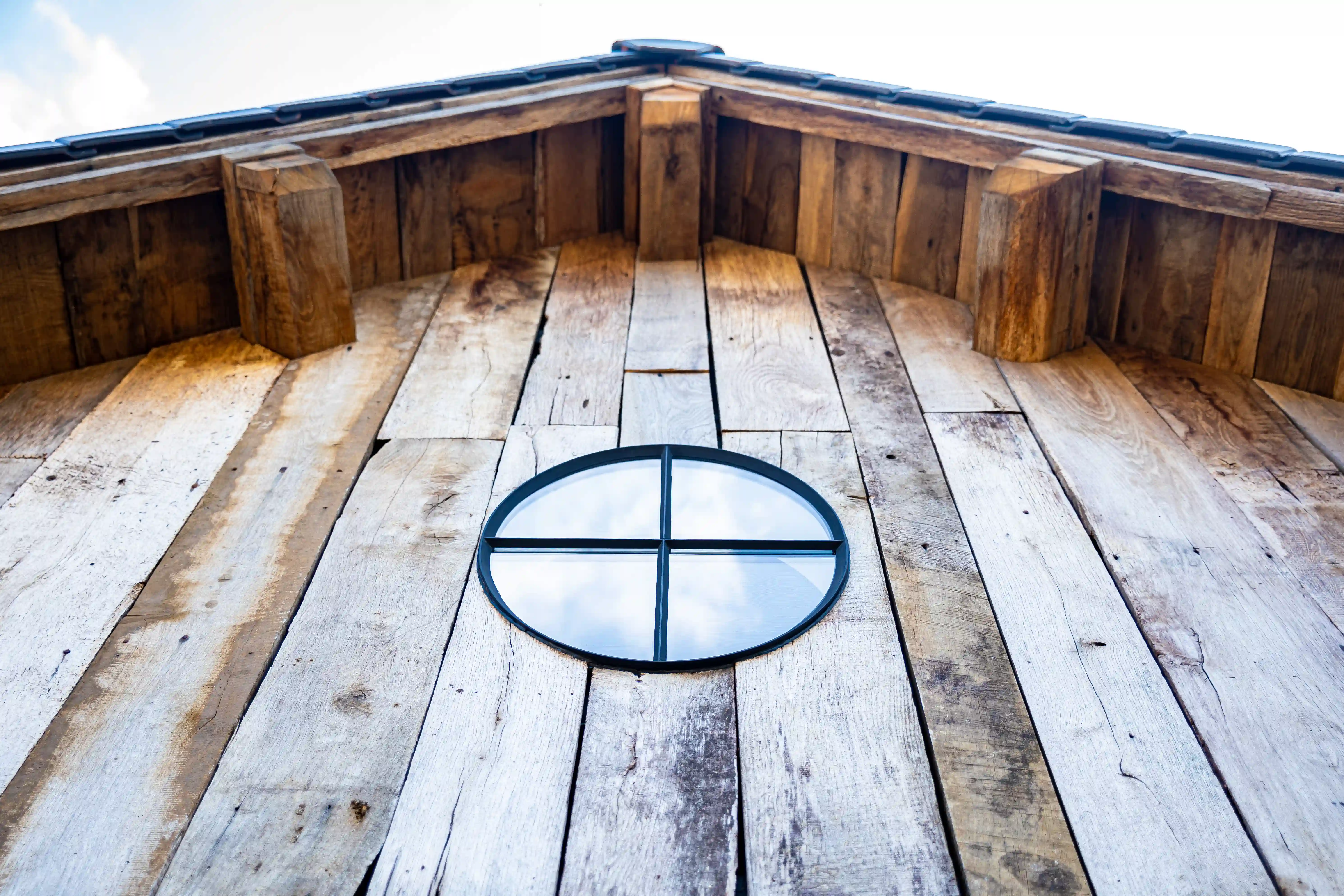 Rustic wooden facade featuring vertical reclaimed timber panels and circular window detail.