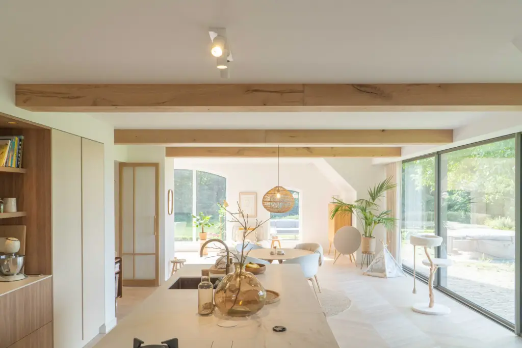 Bright living and dining area in a farmhouse, featuring antique faux wood beams and large windows.