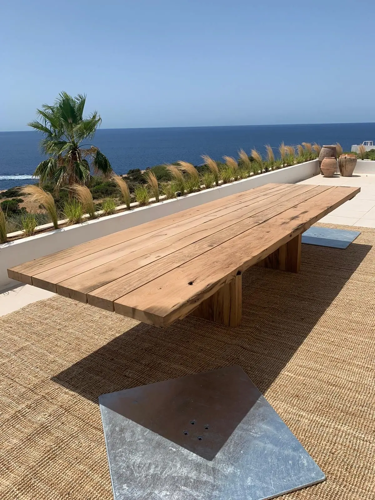 Long reclaimed oak dining table on a sunny terrace overlooking the sea