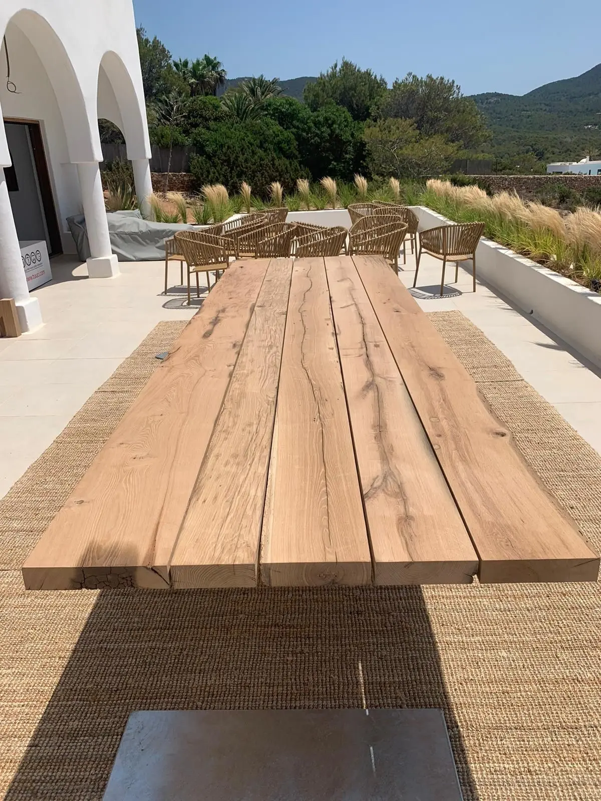 Long reclaimed oak outdoor dining table on a sunny terrace, showcasing the natural character of old oak