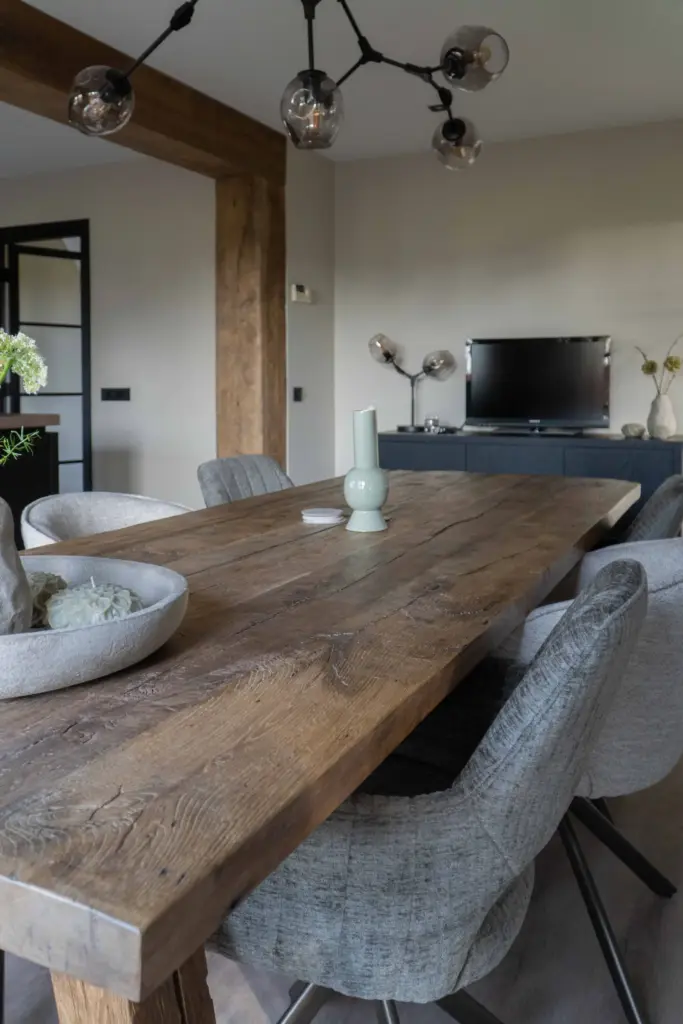 Large reclaimed oak dining table with a naturally weathered surface, surrounded by upholstered chairs in a warm modern interior.