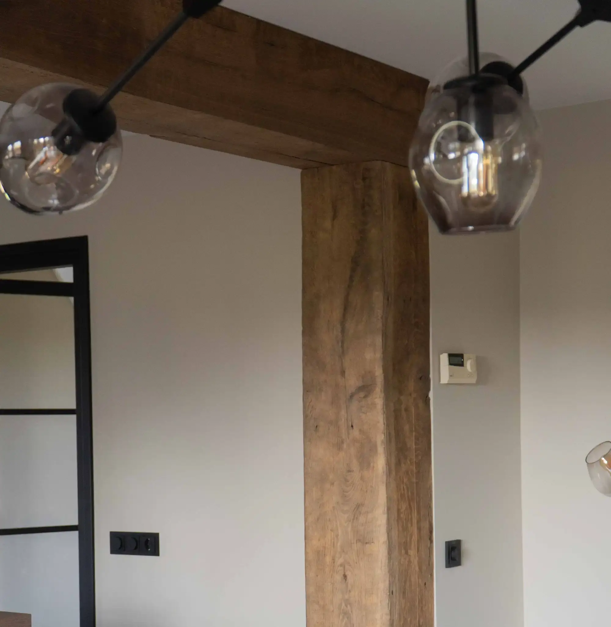 Reclaimed oak beam cladding around a doorway in a warm, modern interior with glass pendant lights.
