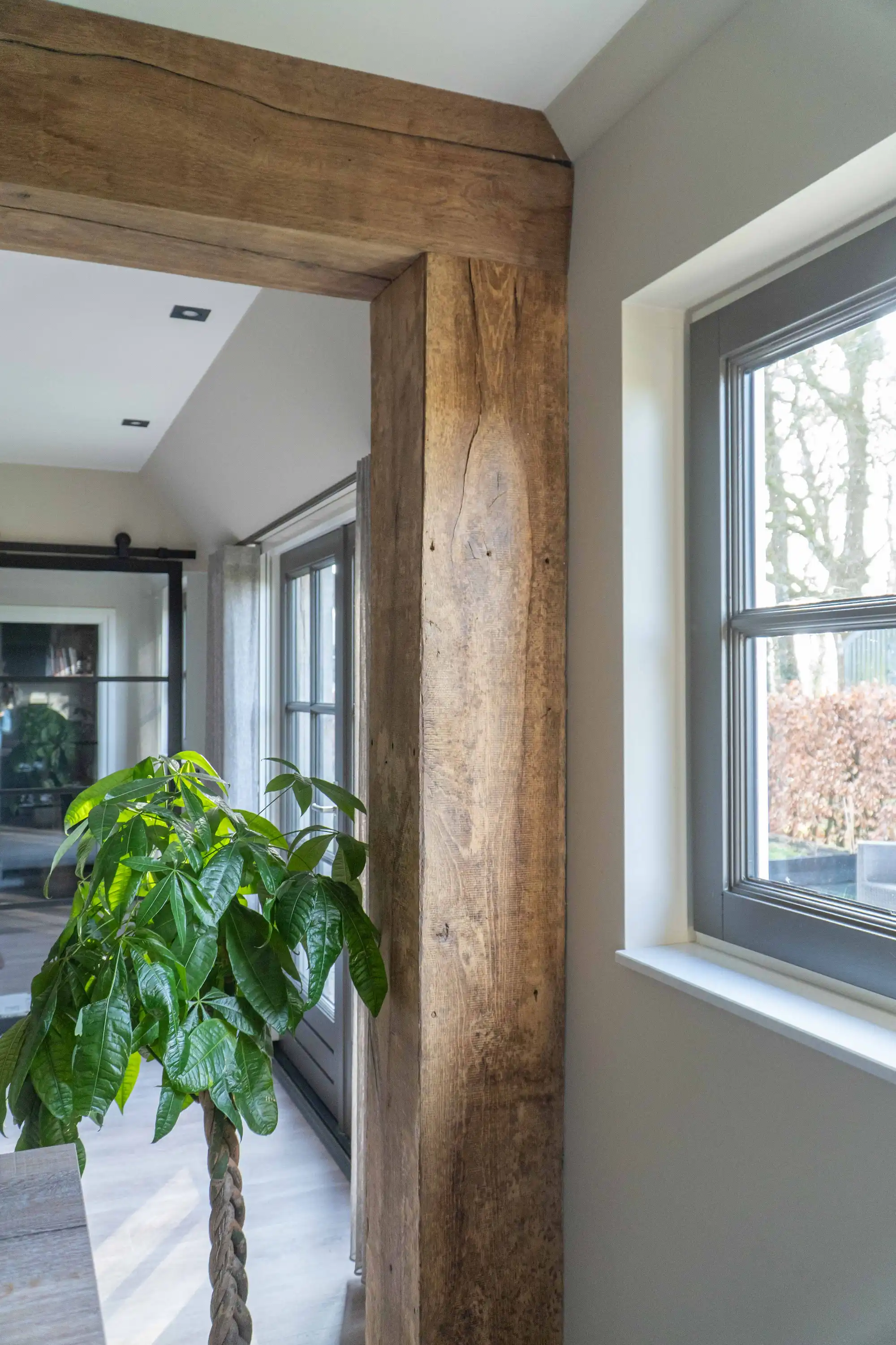Reclaimed oak beam cladding around a doorway in a bright interior with a large window and houseplant.