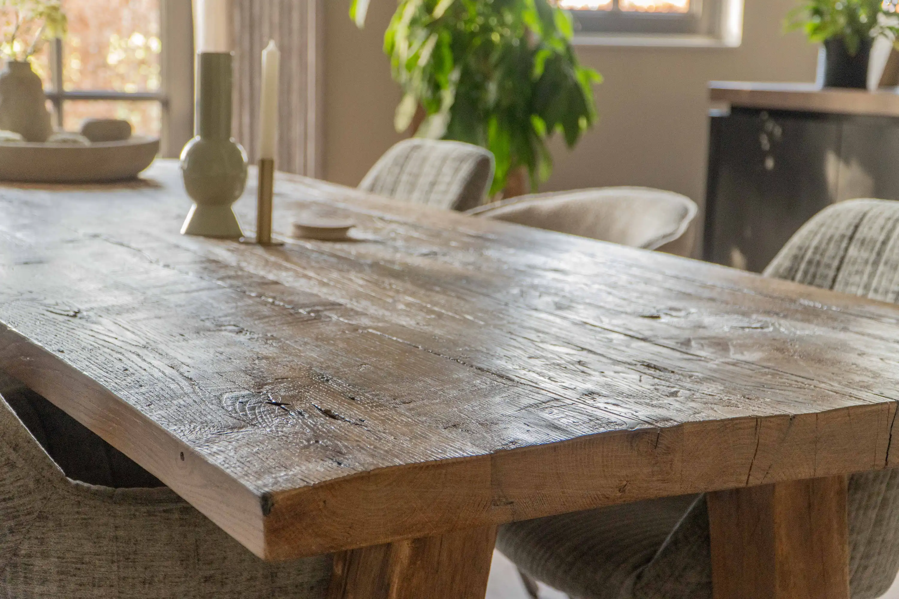 Rustic reclaimed oak dining table with a weathered surface in a bright, modern interior.
